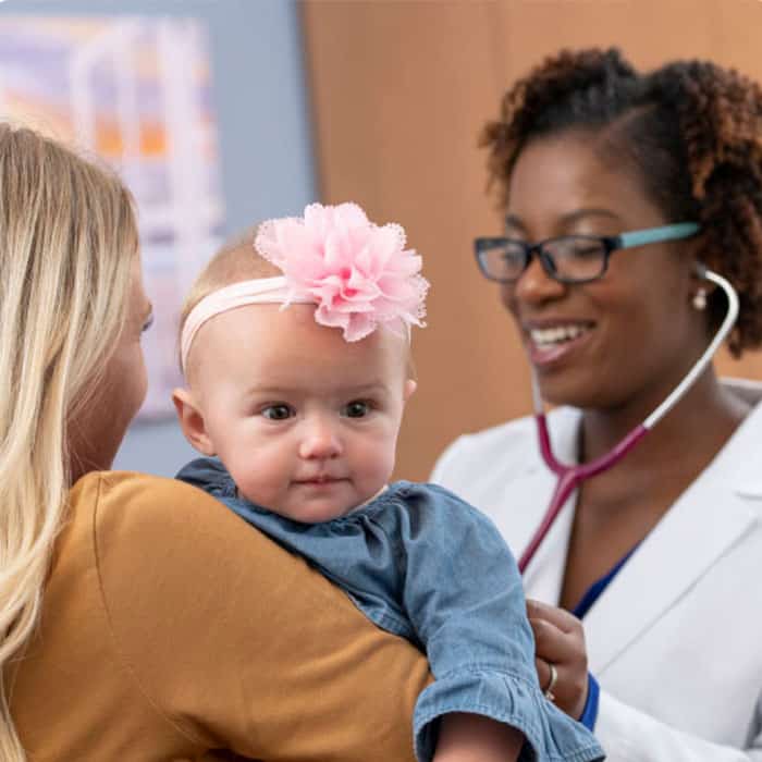 a mom holds her baby girl as a pediatrician examines her