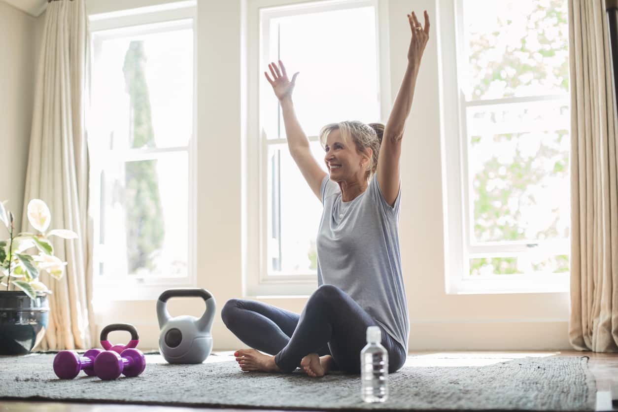 Smiling mature woman with hands raised doing yoga